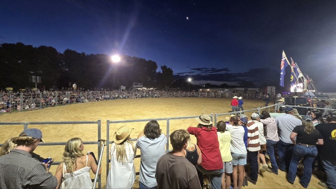 Crowd lining the arena fence under lights at the Hatherleigh Rodeo