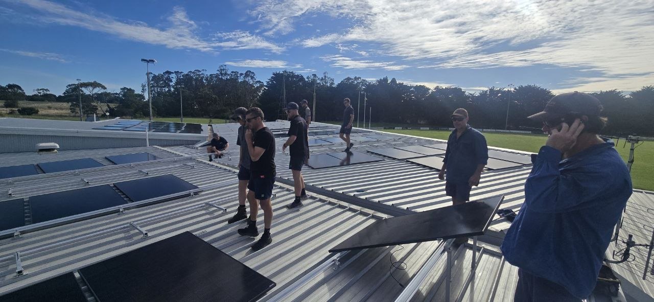 Volunteers on the clubrooms roof installing the new solar panels, with the Hatherleigh oval behind